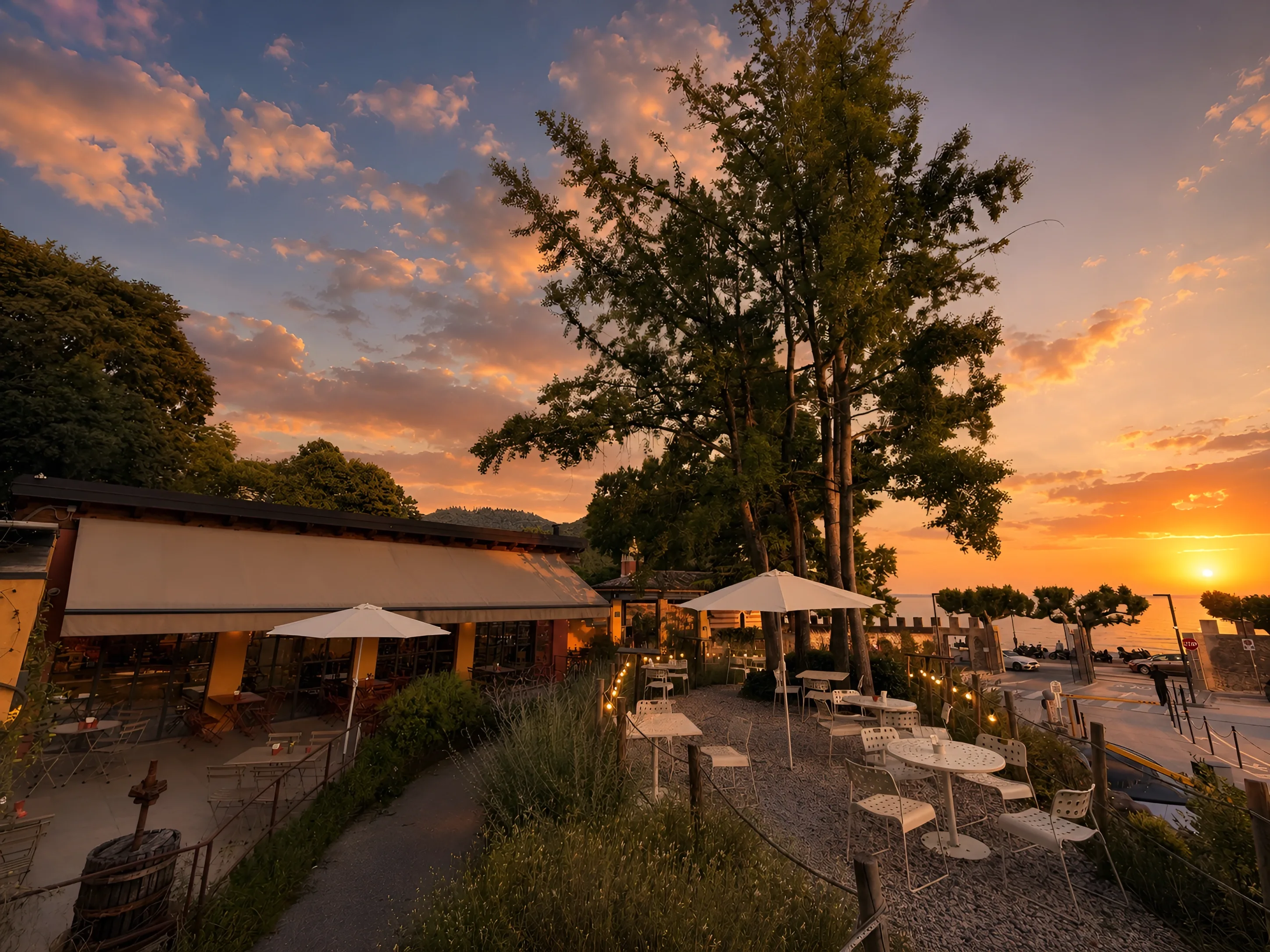 Hortus al tramonto: la terrazza del giardino, gli ombrelloni e le luci sospese mentre il sole scende sul lago di Garda